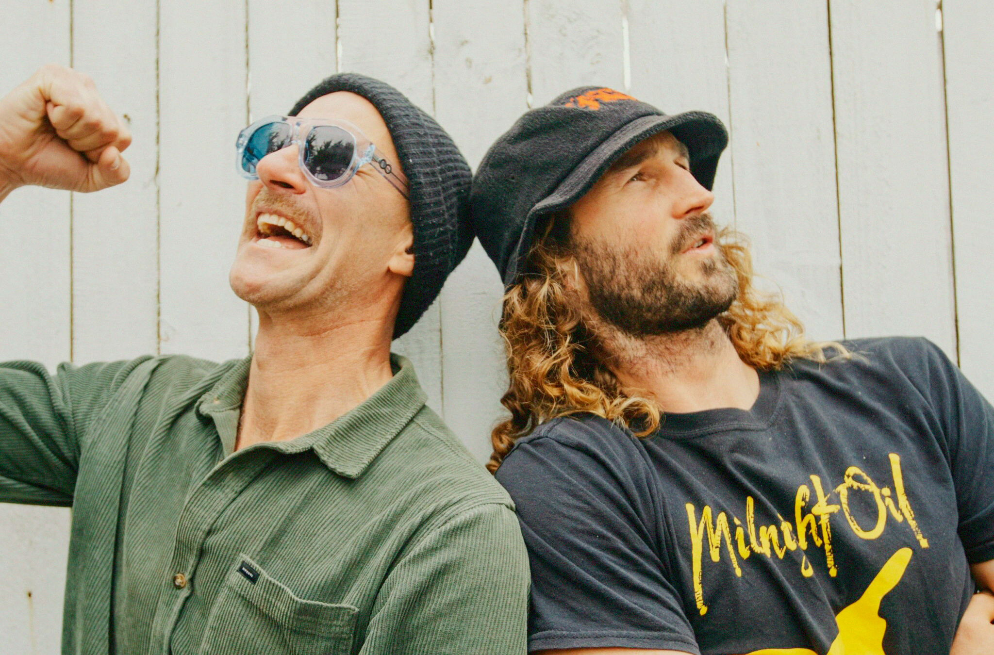 Two men back to back laughing.